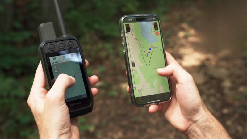 A hunter holds a Garmin handheld device and a smartphone, both showing GPS maps used to track dogs in the field